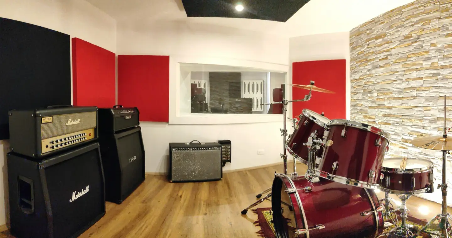 Sala de grabación de Fonosónico: batería roja, cabezales Marshall, paneles acústicos rojos y ventana a la sala de control